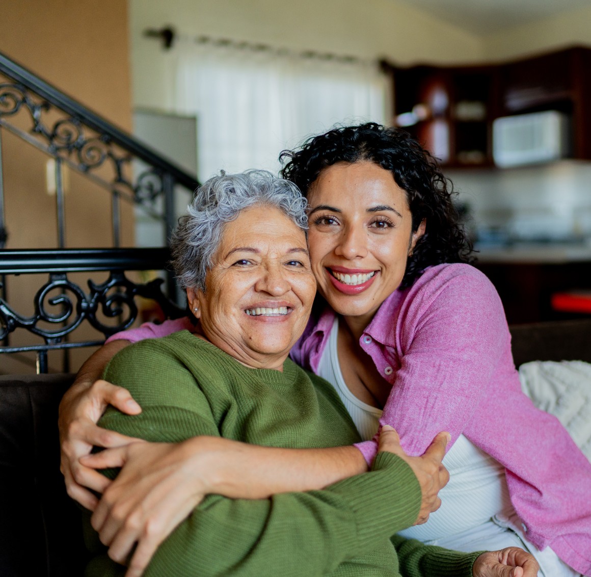 Adult daughter hugging senior mother by staircase Adult daughter hugging senior mother by staircase
