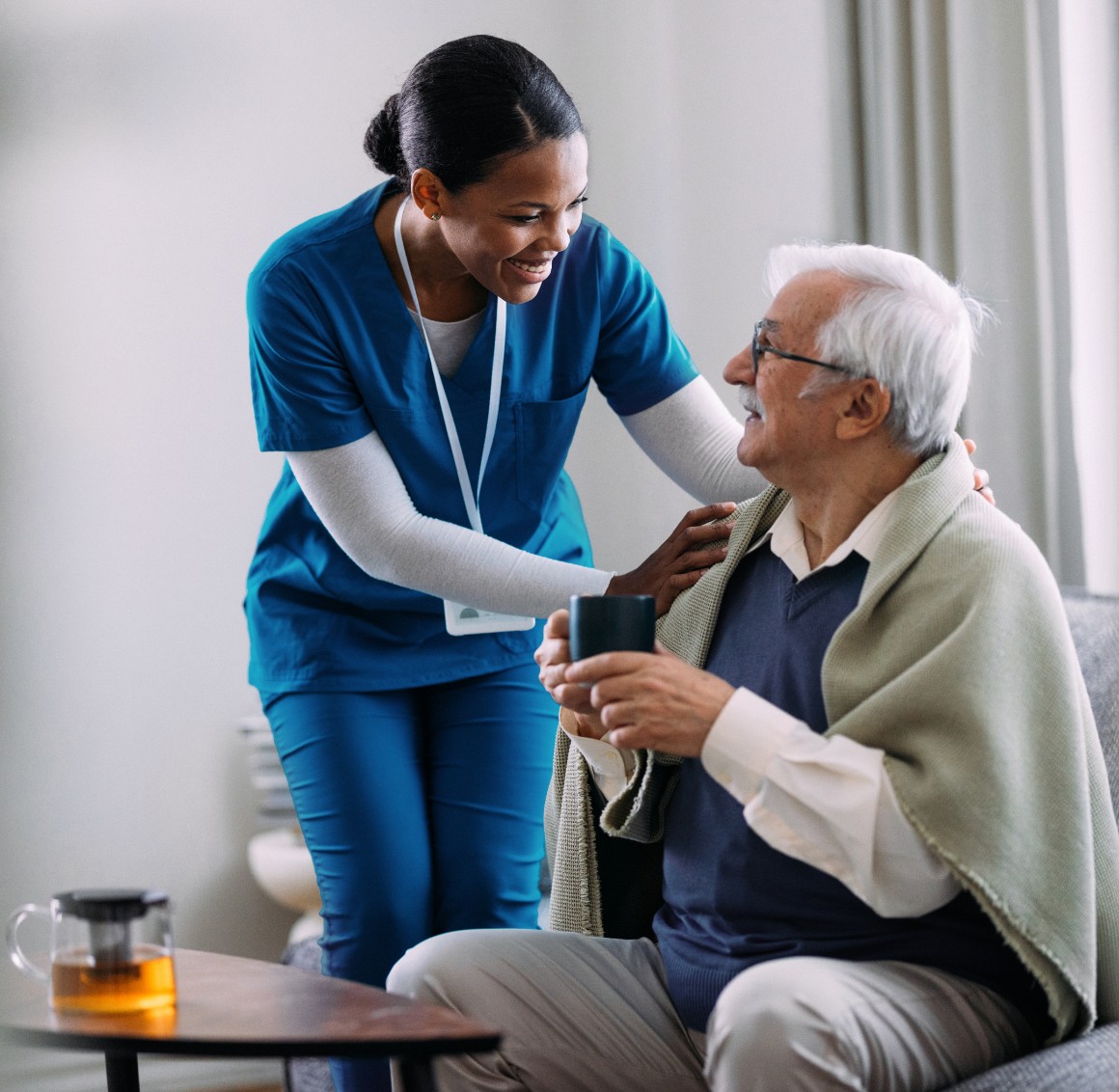Caregiver comforting senior man with blanket and drink – Respite Care Caregiver comforting senior man with blanket and drink - Respite Care
