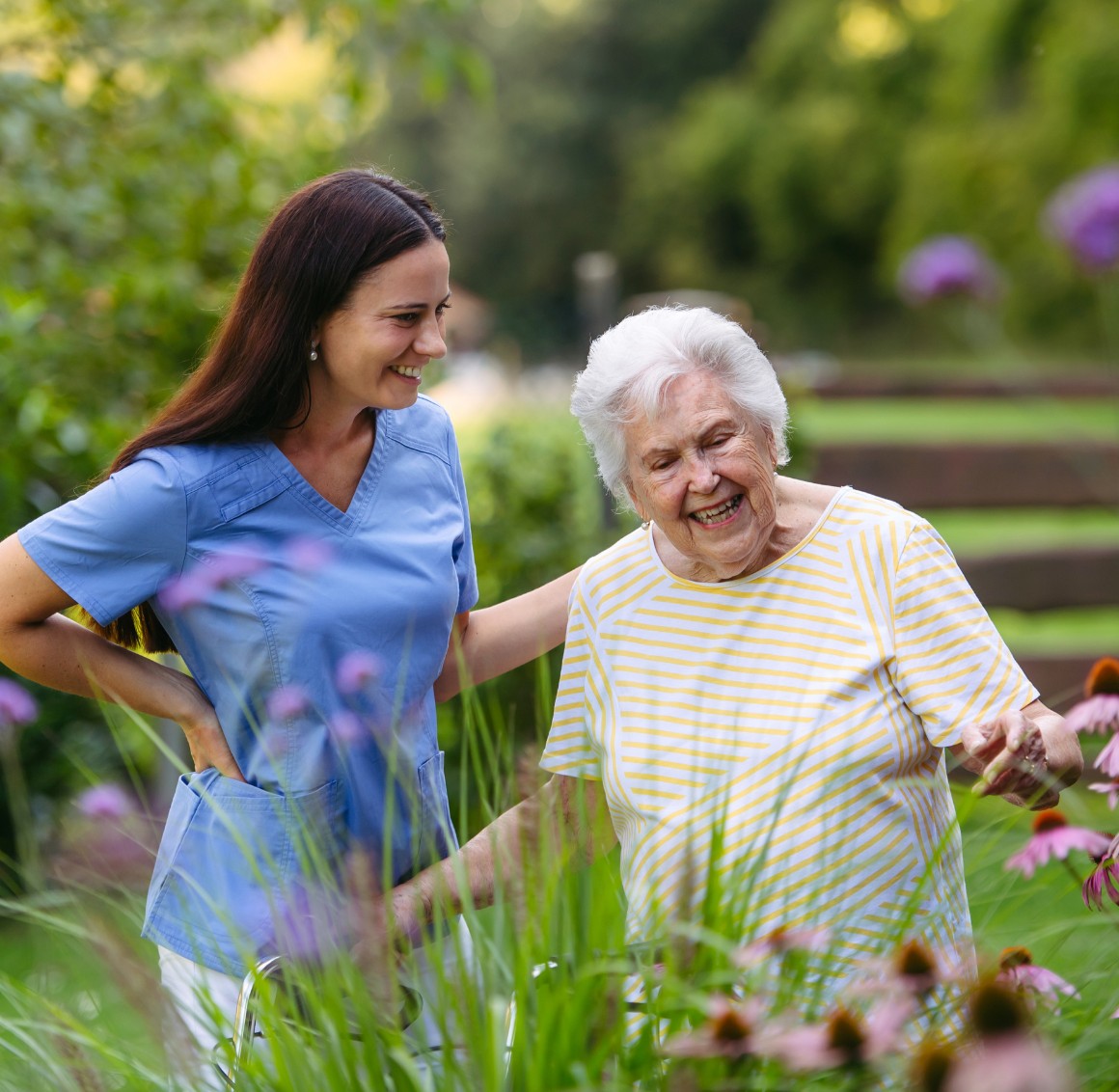 Caregiver helping senior woman walk in garden Caregiver helping senior woman walk in garden